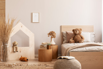 Beige kid's room with wooden nightstand with flowers and books and single bed with teddy bear