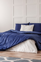 White pillow in the middle of king size bed with blue duvet, copy space on empty wall