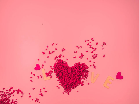 Closeup of red heart shape of small gravel , wooden alphabet love word, pink heart shape sticker on pink pastel color background. Love, valentine, romance, wedding and honeymoon concept and idea.