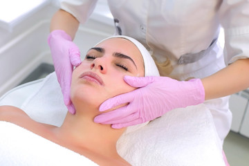 Obraz na płótnie Canvas Cosmetologist in gloves washes client's face, neck and chest with gel. Portrait of young woman, closeup view. Beautician making beauty procedure to patient relaxing in clinic. Beauty industry concept.