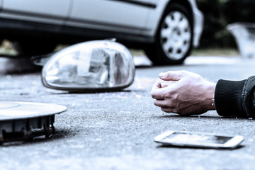 Human's hand on the ground next to broke car mirror and mobile phone after a crash