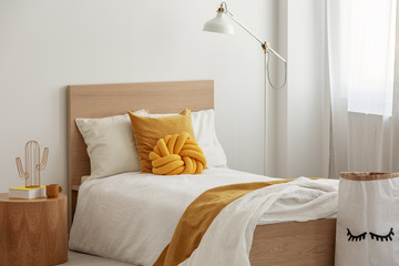 Tall industrial lamp over yellow pillows and blanket on white single wooden bed