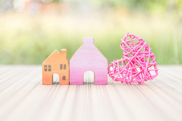 Miniature house with pink heart over blurred green garden background, outdoor day light, home and property business concept