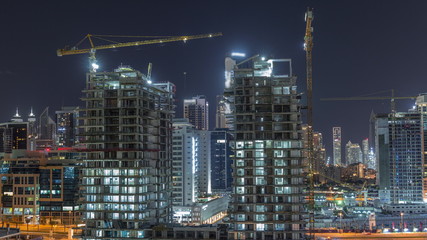 Obraz premium Aerial view of a skyscrapers under construction with huge cranes night timelapse in Dubai.