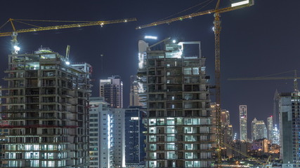 Aerial view of a skyscrapers under construction with huge cranes night timelapse in Dubai.