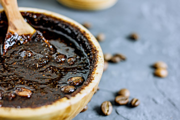Coffee scrub in a wooden bowl with a wooden spoon on a dark stone background. Nearby is a bowl with coffee grounds, coffee grains. Coffee grounds body scrub. Close-up of mine space.