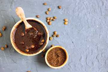 Coffee scrub in a wooden bowl with a wooden spoon on a dark stone background. Nearby is a bowl with coffee grounds, coffee grains. Coffee grounds body scrub. Close-up of mine space.
