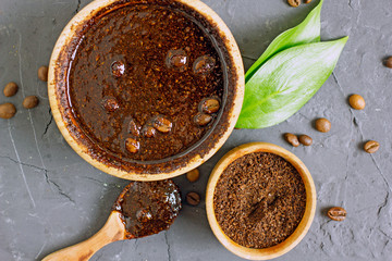 Coffee scrub in a wooden bowl with a wooden spoon on a dark stone background. Nearby is a bowl with coffee grounds, coffee grains. Coffee grounds body scrub. Close-up of mine space.