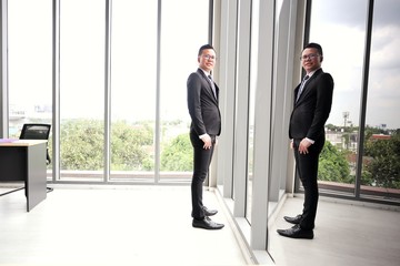 Asian businessmen wearing glasses standing near glass window have reflection in office building
