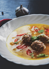 plate of soup with meatballs and vegetables on a dark wooden background