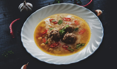 plate of soup with meatballs and vegetables on a dark wooden background