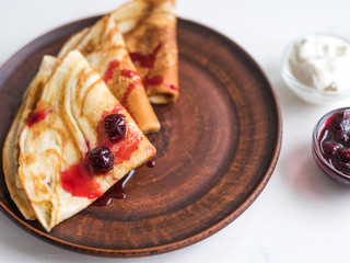 Russian delicious homemade pancakes on a clay plate with yogurt and jam on a bright background, close-up.