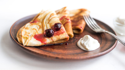 Delicious  russian rustic homemade pancakes on a clay plate with yogurt and jam on a light wooden background, close-up.