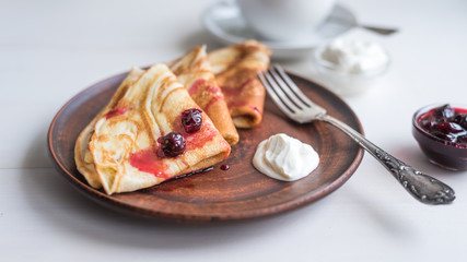 Delicious  russian rustic homemade pancakes on a clay plate with yogurt and jam on a light wooden background, close-up.