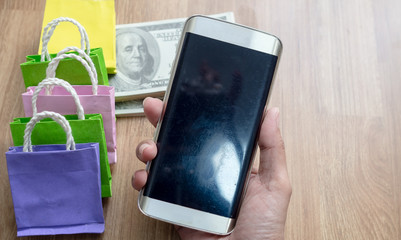 Hand holding mobile phone with  Colorful shopping small paper bag. Concept Ordering online products via the internet from the phone and paying via credit card.