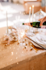 New Year 2019. Table with a gold tablecloth, decorated with candles and tableware for celebration. Festive still life by candlelight. Bengal lights in the foreground. Man pours champagne.