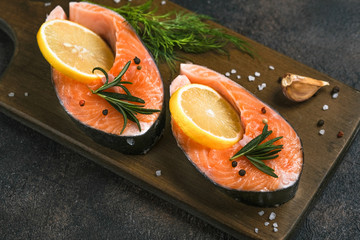 Fresh salmon steaks with herbs, lemon, rosemary and spices on a cutting board on a dark background.