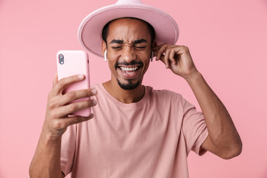 Photo of laughing african american man using cellphone and earpods