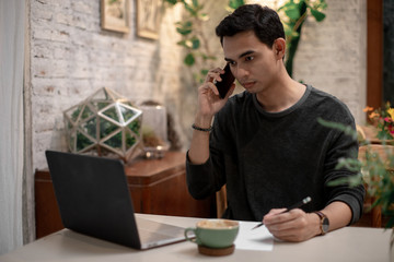 a man is working in his house and drinking coffee and using his mobile talking to his co worker
