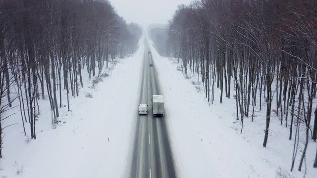 Aerial view of traffic on a road surrounded by winter forest in snowfall