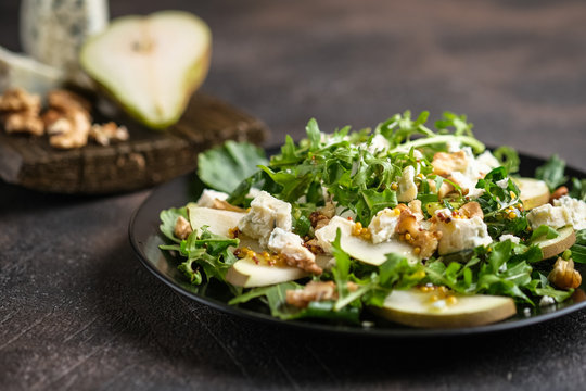 Salad Of Pear, Blue Cheese, Arugula And Nuts With Spicy Dressing On A Dark Background. Healthy Eating.