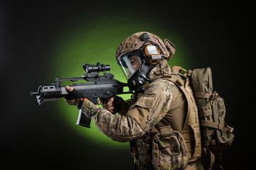 a male soldier in military clothes with a weapon on a dark background in a gas mask