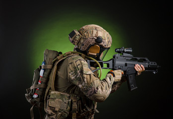 Fototapeta premium a male soldier in military clothes with a weapon on a dark background in a gas mask