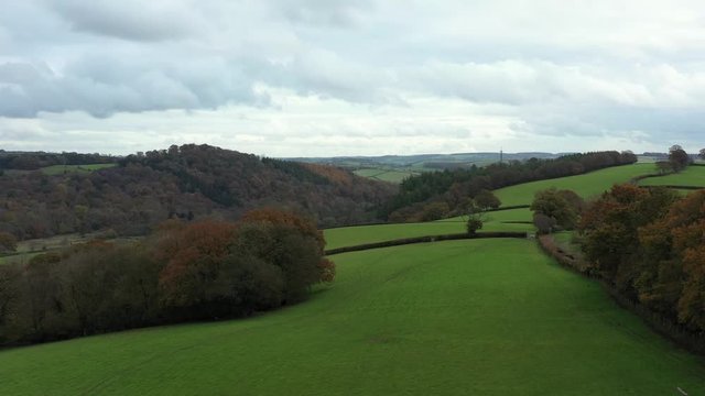 Aerial profile view of autumn trees, footpaths and fields on the hilltop of the valley over the market town of Dulverton in Exmoor.
