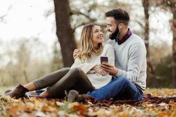 Happy couple enjoying in autumn day and listening music on smart phone