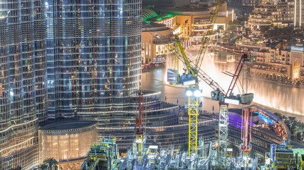 Obraz premium Aerial view of a skyscraper under construction with huge cranes night timelapse in Dubai.