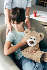 cropped view of child psychologist hugging kid with dyslexia holding teddy bear