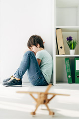 selective focus of sad kid with dyslexia sitting on floor - obrazy, fototapety, plakaty