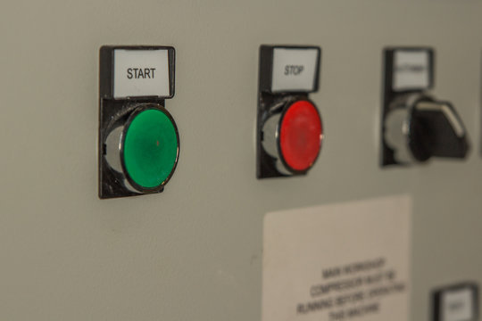 A Bright green start button on an industrial machine working in a factory switches on a white background. Electrical devices for production and stop buttons for health and safety.