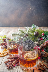 Christmas winter alcohol drink. Orange, spice and bourbon whiskey alcoholic cocktail in two glasses, wooden background with christmas tree branches and decor, copy space