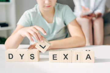 cropped view of kid with dyslexia sitting at table and playing with wooden cubes - obrazy, fototapety, plakaty