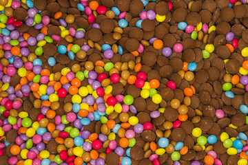 An endless montage of colourful smarties both covered in sweets candy coating and uncoated straight chocolate sweets. Pink, purple, green, blue, yellow lovely background but unhealthy.