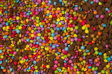 An endless montage of colourful smarties both covered in sweets candy coating and uncoated straight chocolate sweets. Pink, purple, green, blue, yellow lovely background but unhealthy.