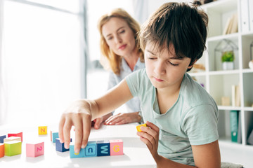 selective focus of kid with dyslexia playing with building blocks and child psychologist looking at it on background