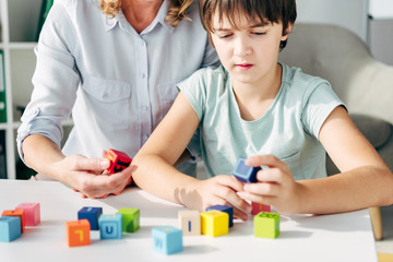 cropped view of child psychologist and kid with dyslexia playing with building blocks