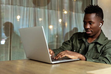 Cheerful young african american man in headphones using computer in cafe