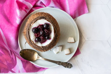 Berry dessert with yogurt in a cup of coconut on a light background. Blackberries, raspberries, blueberries, black currants. Pink napkin
