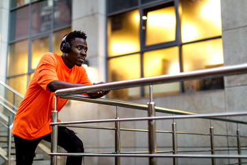 african-american man in stylish orange hoodie sweatshirt in wireless headphones listening music outdoor in the evening. copy space