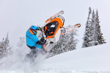 A man is riding snowmobile in mountains. jump on a snow bike. pilot on a sports snowmobile in a mountain forest. The concept of skidooking. rider in a bright suit on a colorful snowy moto. Hi quality
