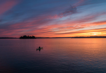 A lone kayaker contemplates the meaning of life while in a meditative moment out in the middle of a calm lake under a colorful northern sky.