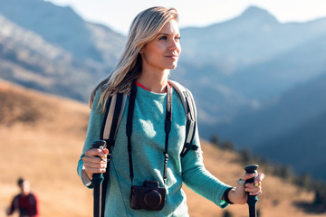 Pretty young woman traveler with backpack looking to the side while walking on mountain. - obrazy, fototapety, plakaty