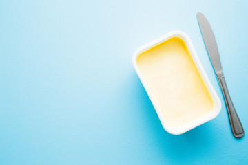 Opened plastic pack of light yellow margarine and knife. Closeup. Empty place for text or logo on pastel blue desk. Top down view.  - obrazy, fototapety, plakaty