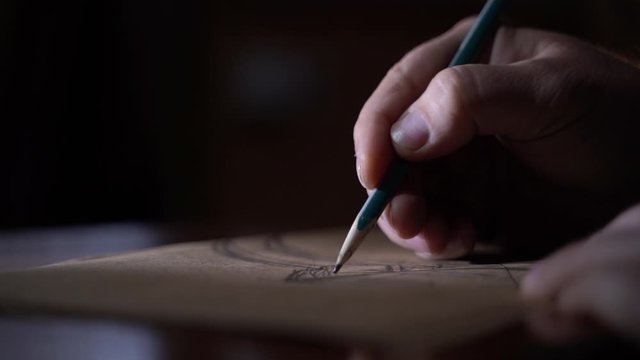 Man draws the design of future wood furniture in a luxurious style in dark room for concentration Close-up 4K footage
