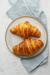 Two delicious croissants on plate and hot drink in mug. Morning French breakfast with fresh pastries. Light gray background, vertical
