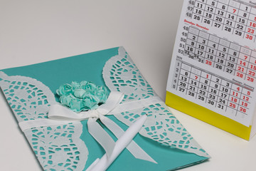 Handmade greeting card made of green paper. Decorated with braid and green flowers. Nearby is a fragment of the calendar with the month of December.