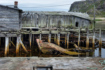 Russia, Arctic, Kola Peninsula, Barents Sea, Teriberka: Run down abandoned wooden houses at old fishing harbor in the city center of the Russian settlement small fishing village - lost place travel